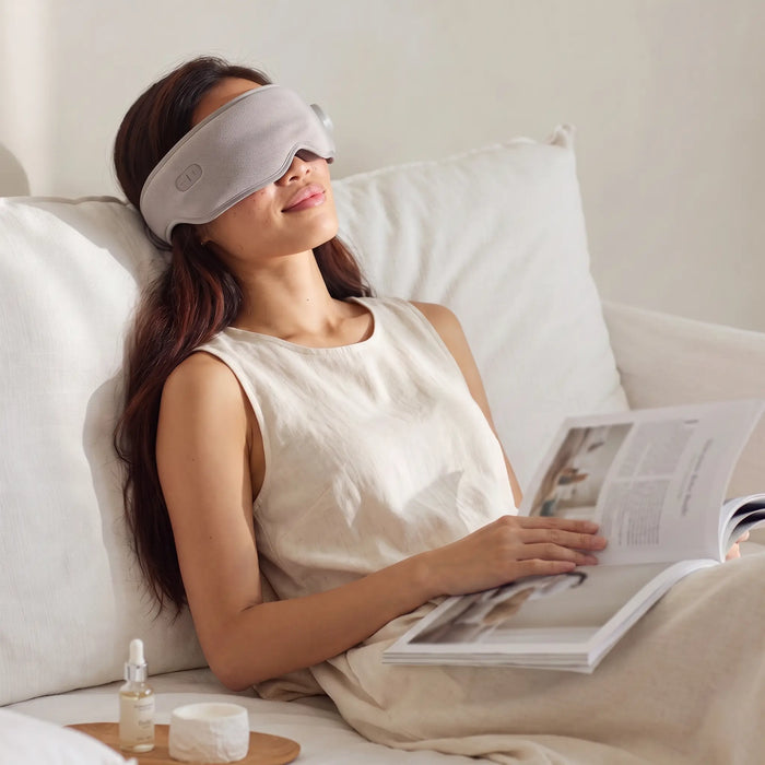 Woman resting on a sofa wearing the light-grey heated eye massager
