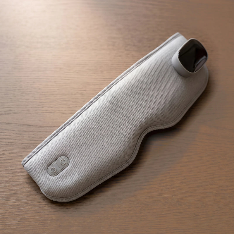 The Unwind heated eye massager in Light Grey on a smoked oak table