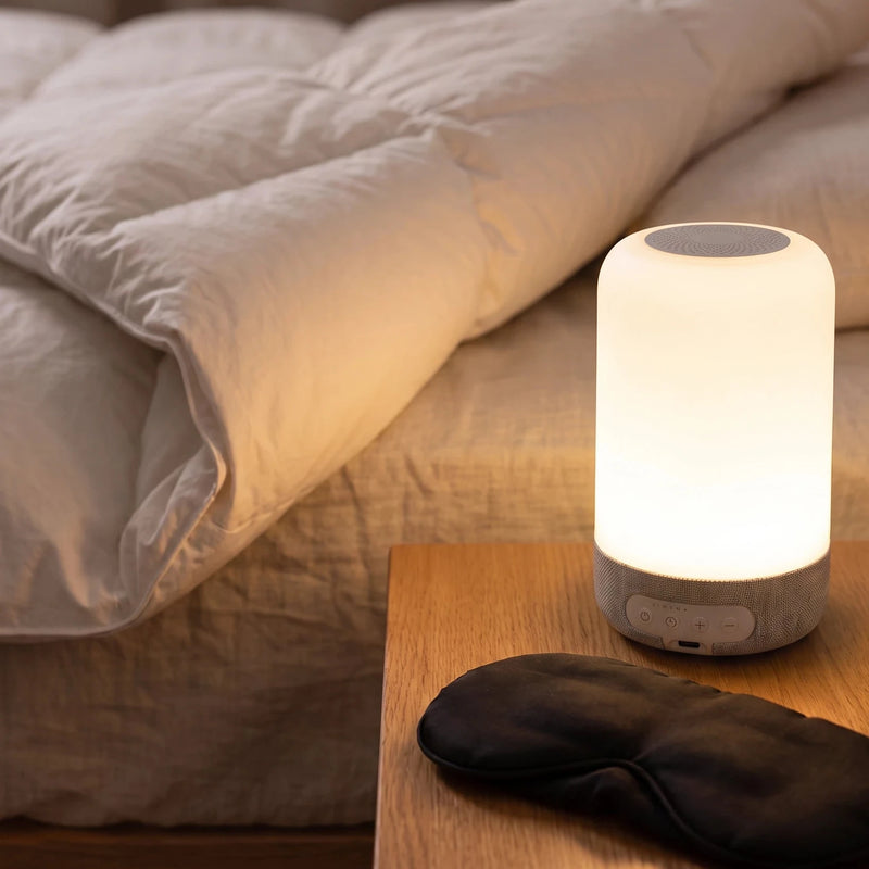 The bedside lamp lit at bedside, a sleep mask beside it for scale