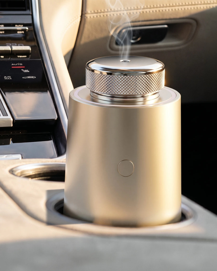 The car diffuser in Champagne Gold in a car's cup holder at sunrise, a fine, cool mist in the light