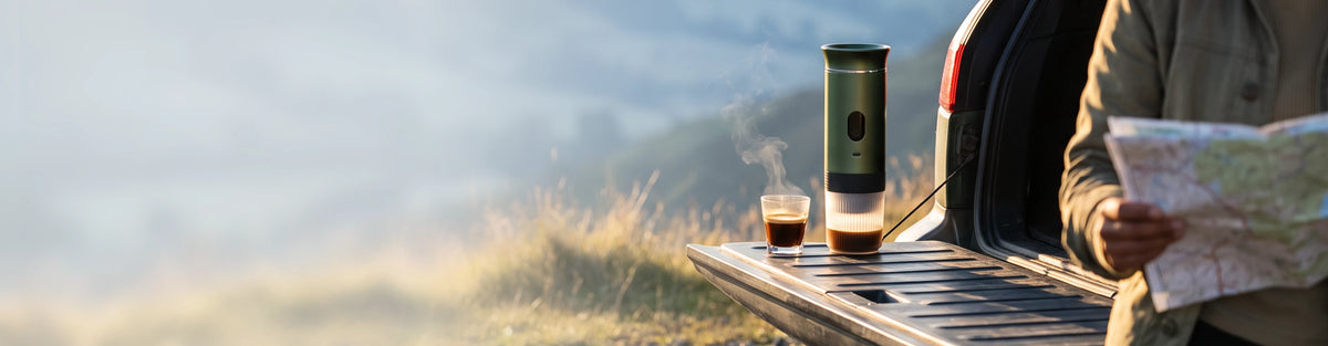 A portable espresso maker and a glass of coffee on a tailgate table above a misty valley at sunrise