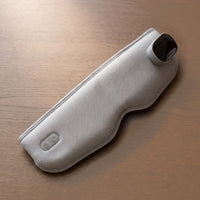 The Unwind heated eye massager in Light Grey on a smoked oak table