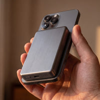 The power bank in dark gunmetal, 10000mAh height, held on the back of a dark grey phone, its blank side outward
