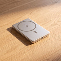 The power bank in natural brushed aluminum, alone on pale oak, seen from a low three-quarter angle