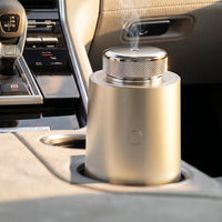 The car diffuser in Champagne Gold in a car's cup holder at sunrise, a little mist in the light