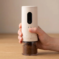 The cordless coffee grinder held in one hand, for scale