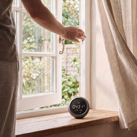 A hand opening a window beside the CO2 monitor on the sill